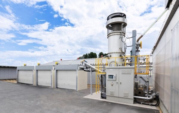 Rendering of Yanmar Rice Husk Biochar Production System with grey industrial plant alongside garage-like units in yard, blue skies behind.