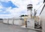 Rendering of Yanmar Rice Husk Biochar Production System with grey industrial plant alongside garage-like units in yard, blue skies behind.